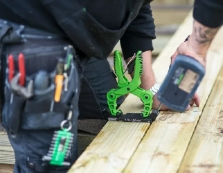 En snickare från Boli Bygg AB använder en grön tving för att fixera träreglar under ett bygge.