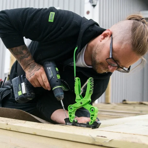 En snickare som använder en skruvdragare och en grön tving under ett husbygge.